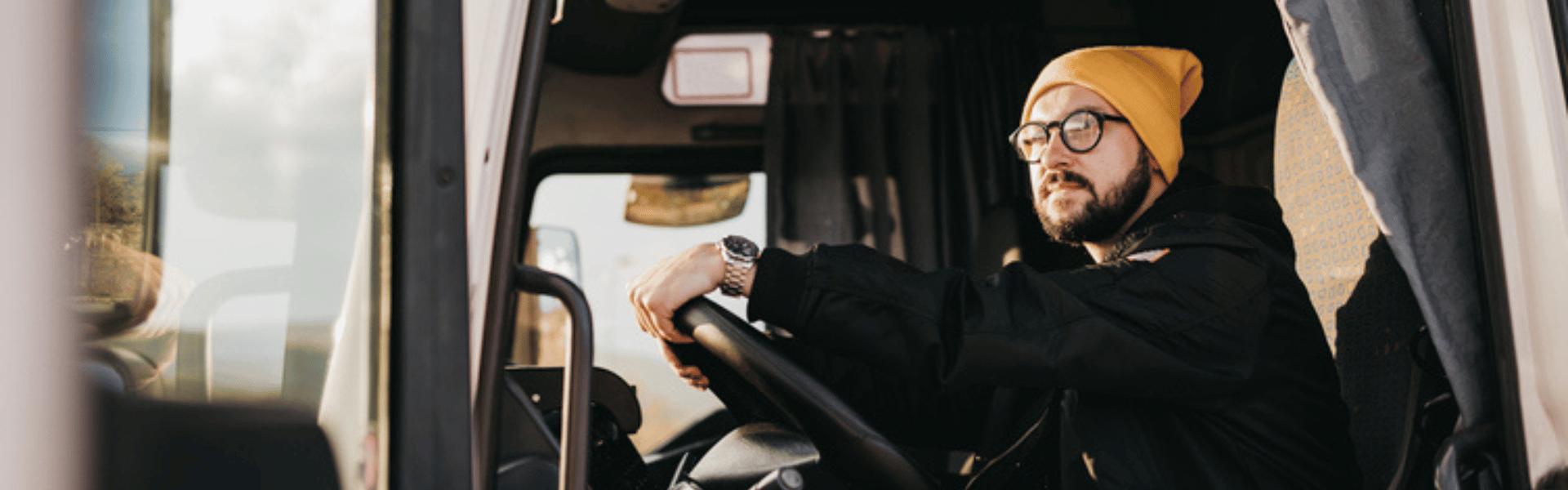 Young man with glasses and stocking hat at the wheel of a semi truck
