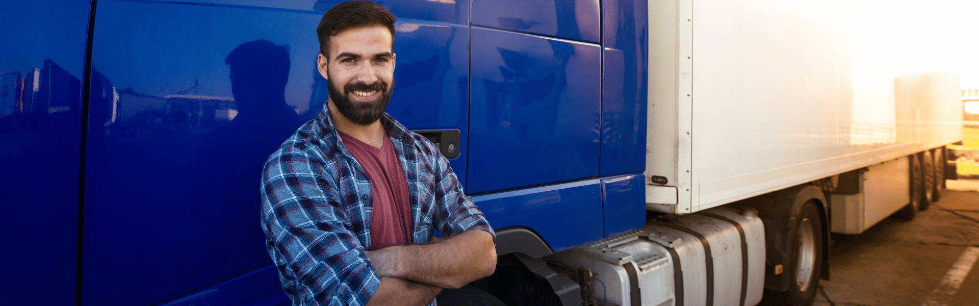 Semi truck driver leaning on semi truck with folded arms