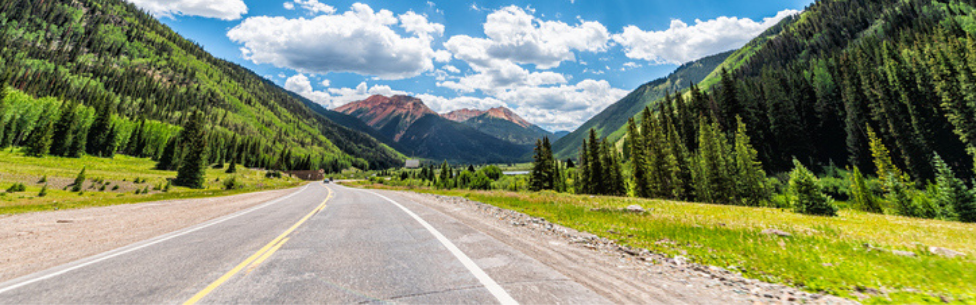 highway in colorado with blue sky and fluffy clouds and mountains