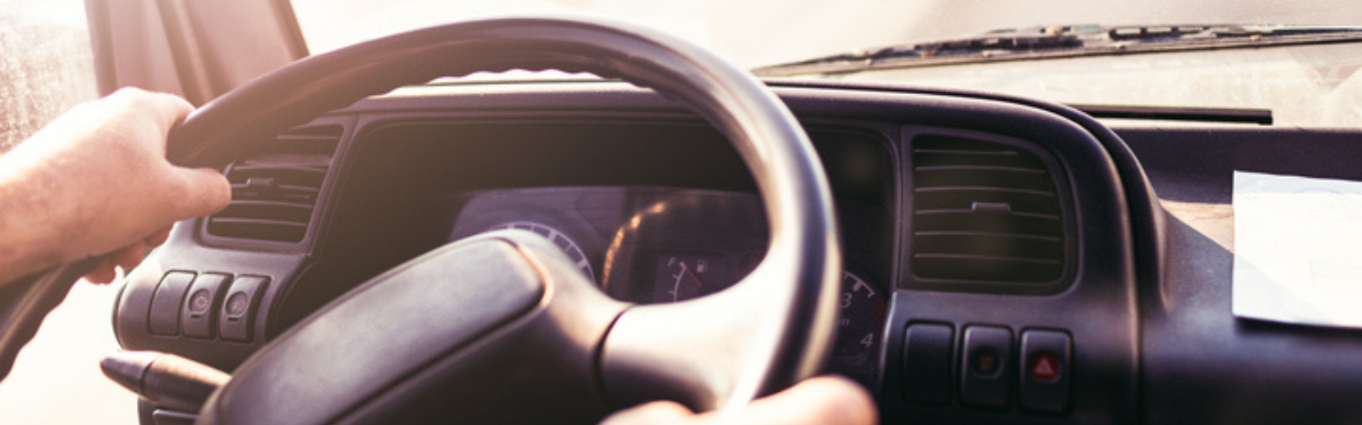 Truck driver in semi truck cab with hands on steering wheel looking out over road through windshield
