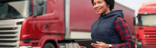 woman holding tablet in front of semi trucks