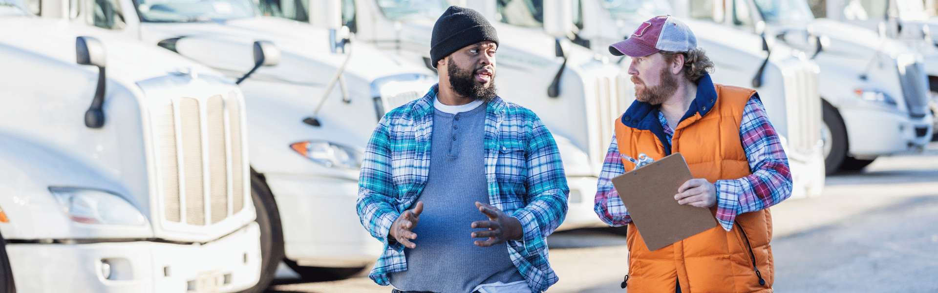 two men talking in front of semi trucks