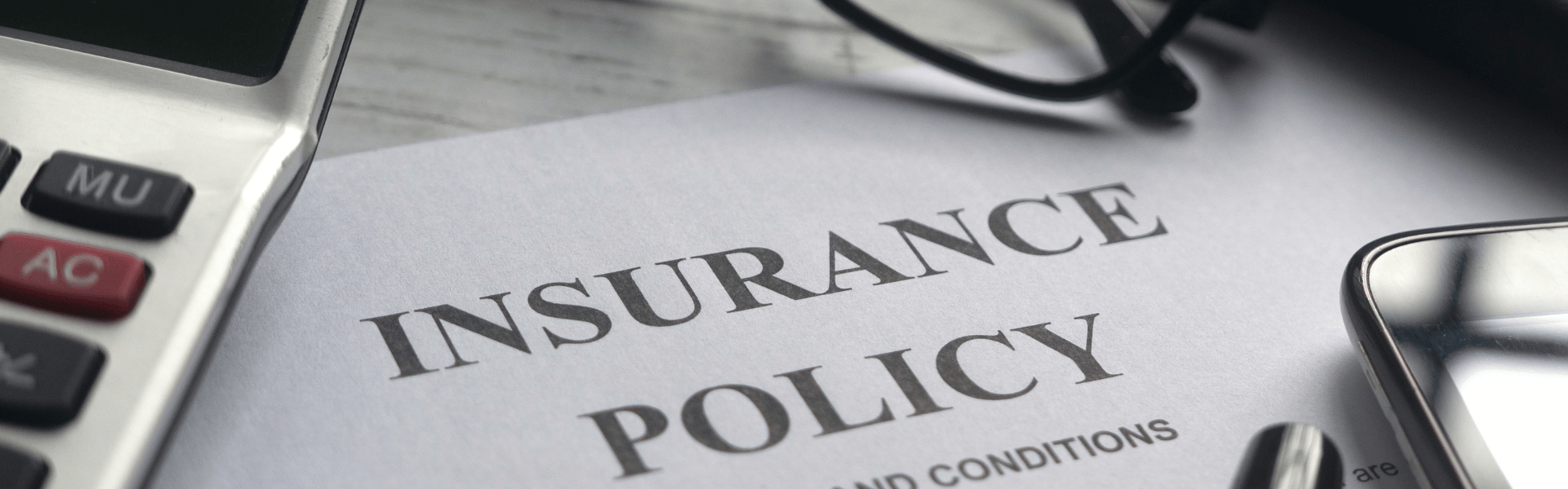 Insurance policy on desk next to calculator and glasses