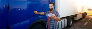 man standing next to semi truck holding up cdl