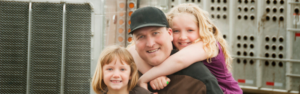 Man with two little girls hugging him in front of semi truck