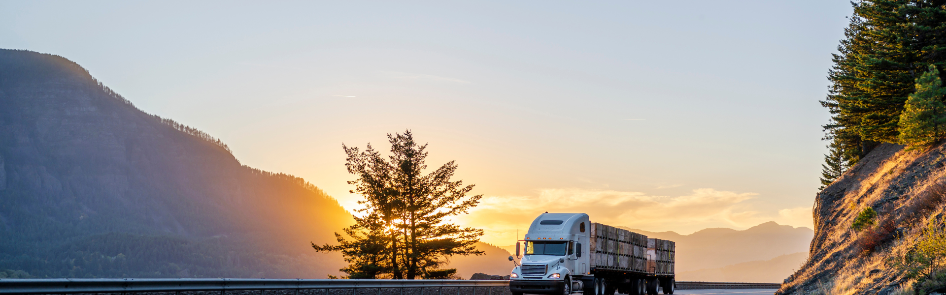 semi truck on highway with mountains, trees, and sunset in background