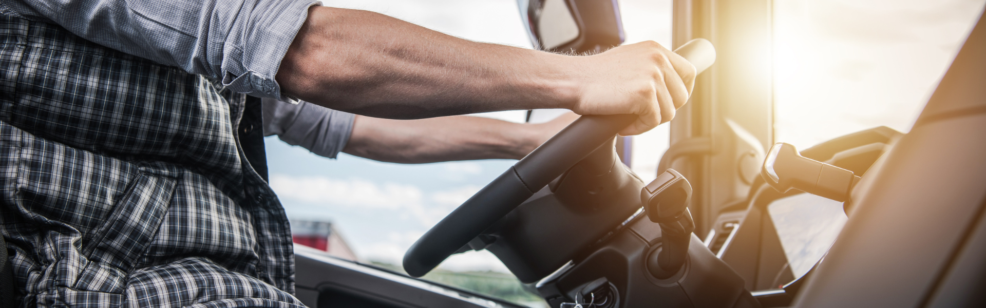 semi truck driver in the cab of a semi truck with sun coming in through windshield
