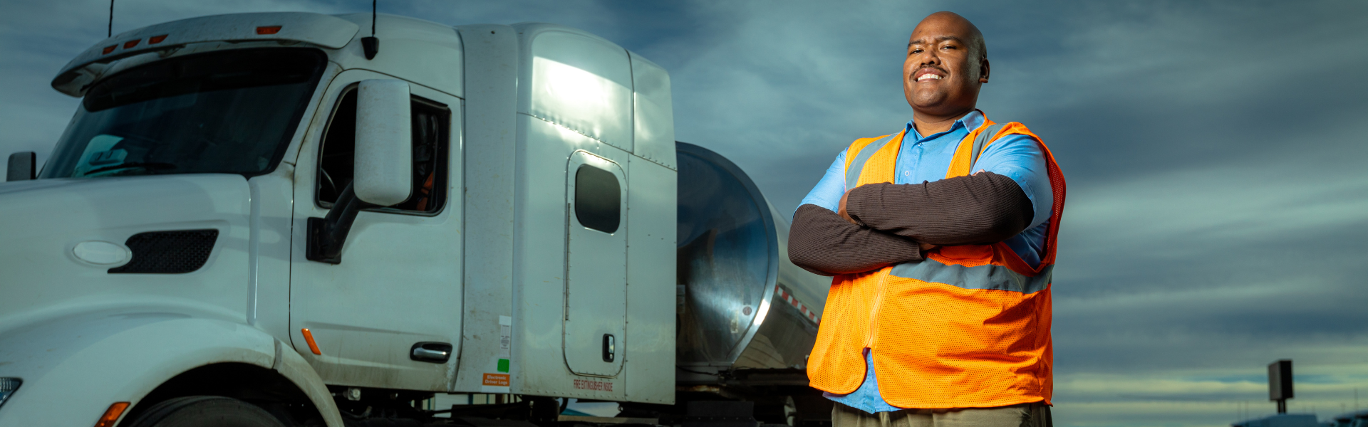 black man standing in front of white semi truck with folded arms