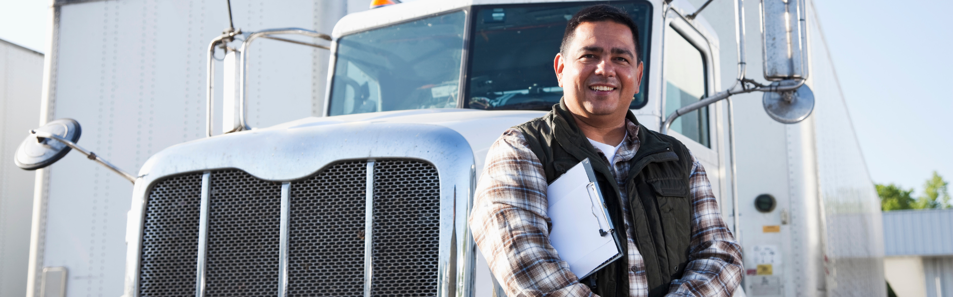 man with clipboard leaning against semi truck