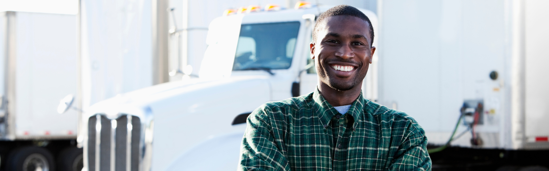 black man in flannel shirt standing in front of semi truck