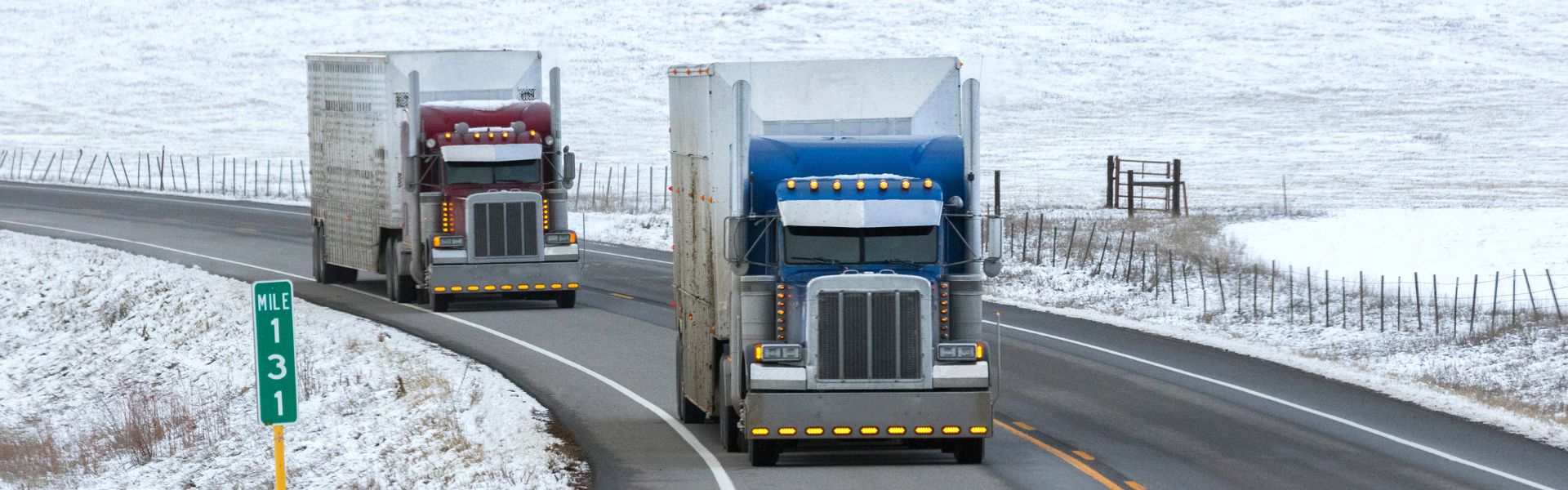 two older semi trucks driving on highway with snowy shoulders