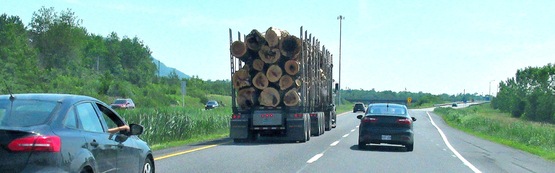 logging semi truck passing car on four lane highway