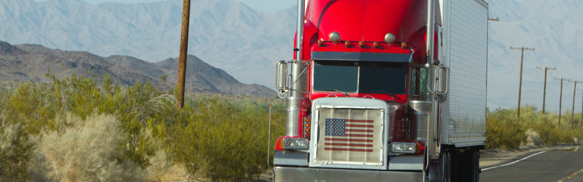red semi truck with american flag in grille on road