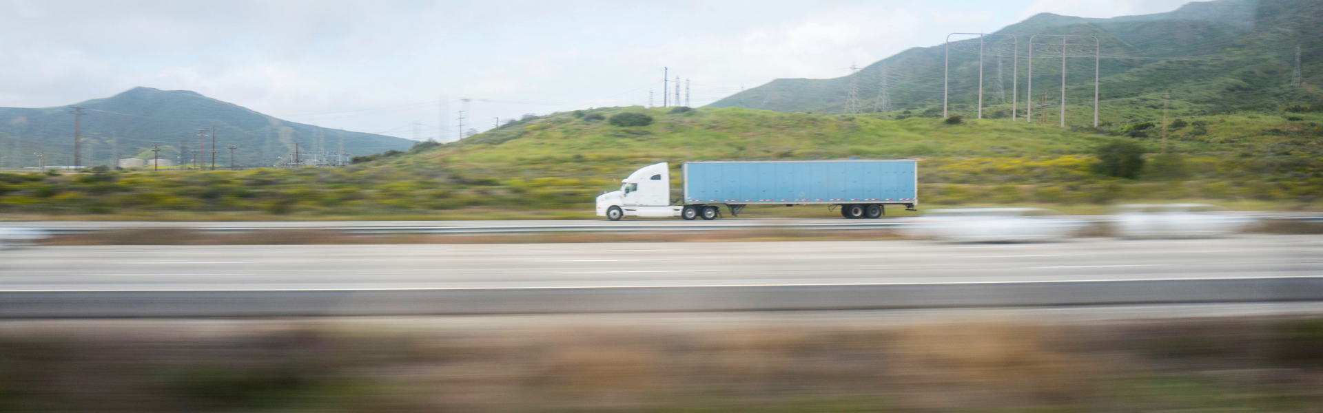 white semi truck with blue trailer on road with mountains in background