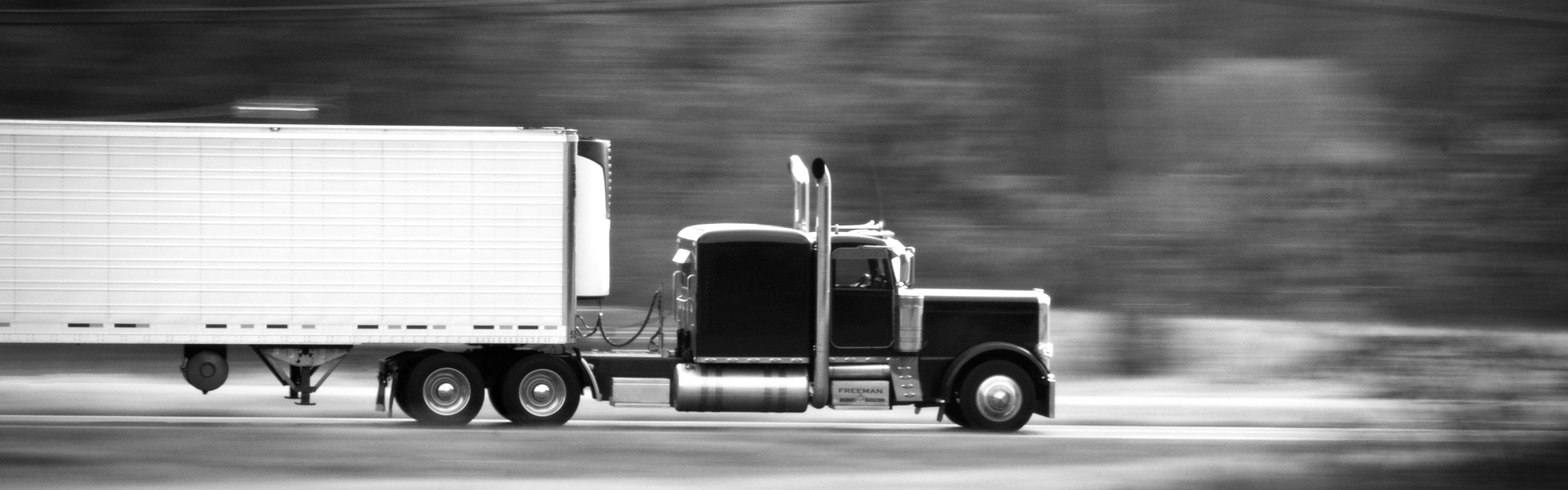 black and white photo of semi truck driving on road