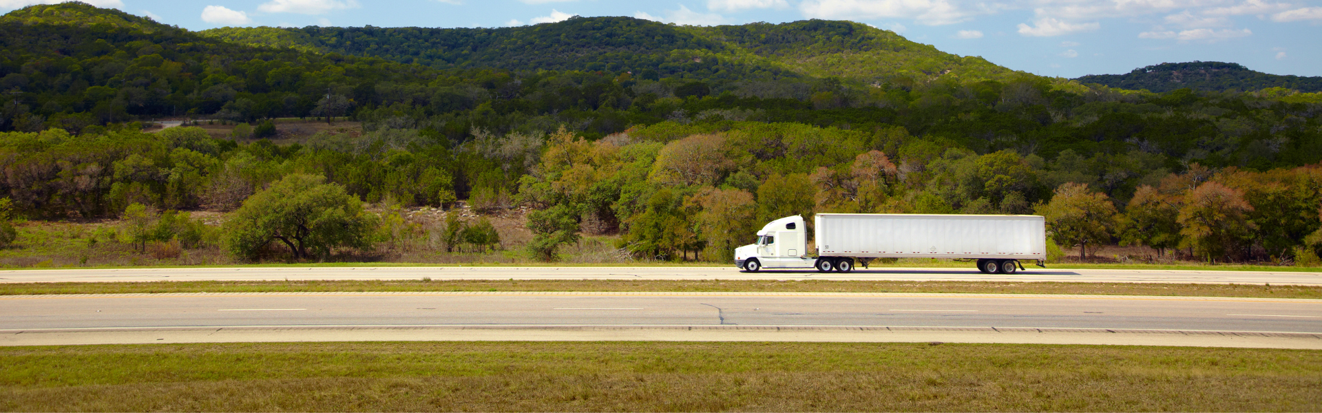white semi truck on road with green rolling hills in background