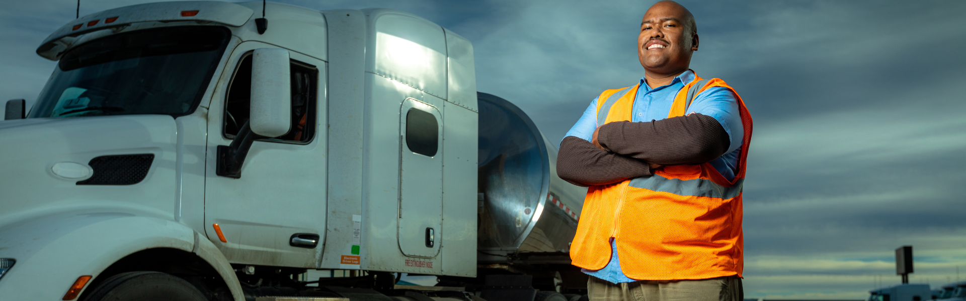 black man standing with crossed arms in front of white semi truck