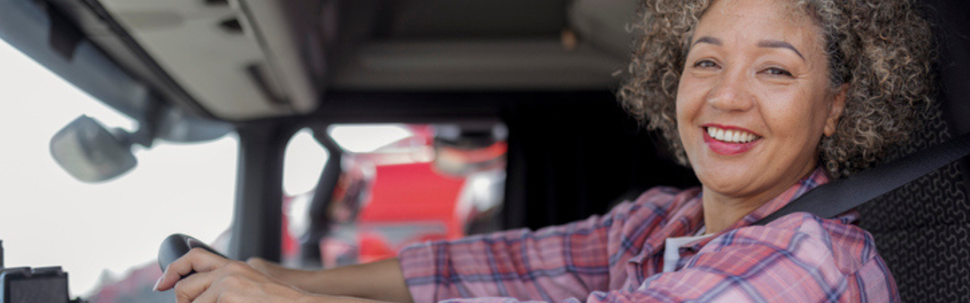 black woman in pick plaid shirt driving semi truck
