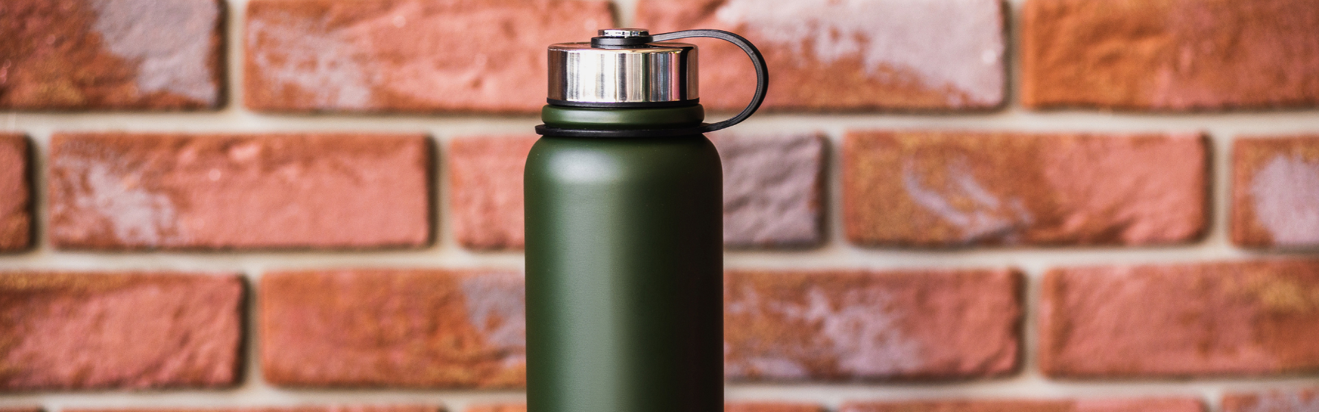 green insulated water bottle with brick wall in background
