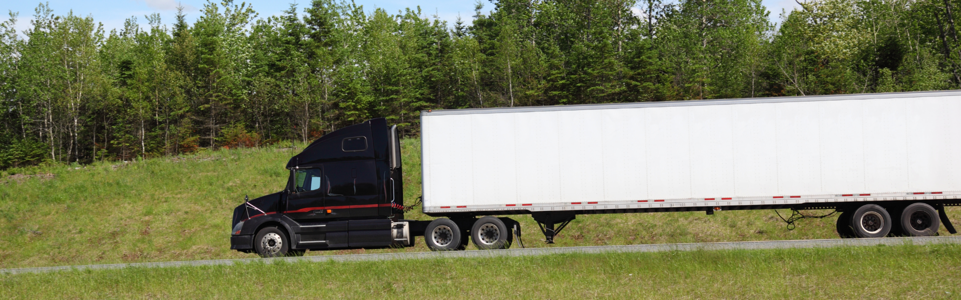 black semi truck with white trailer driving on road surrounded by green grass