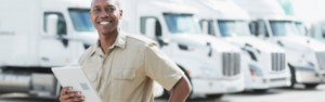 black man with tablet in front of white semi trucks