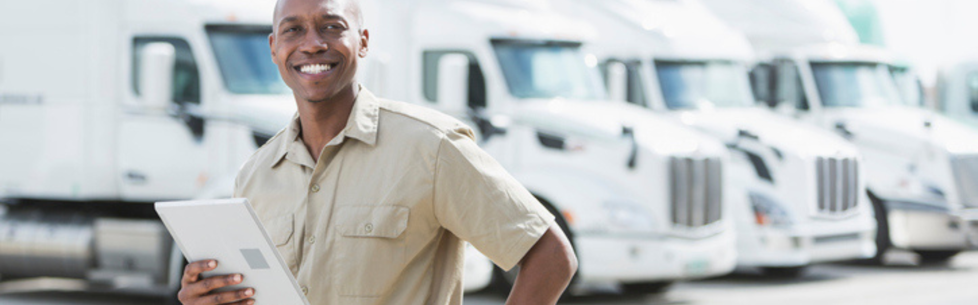 black man with tablet in front of white semi trucks