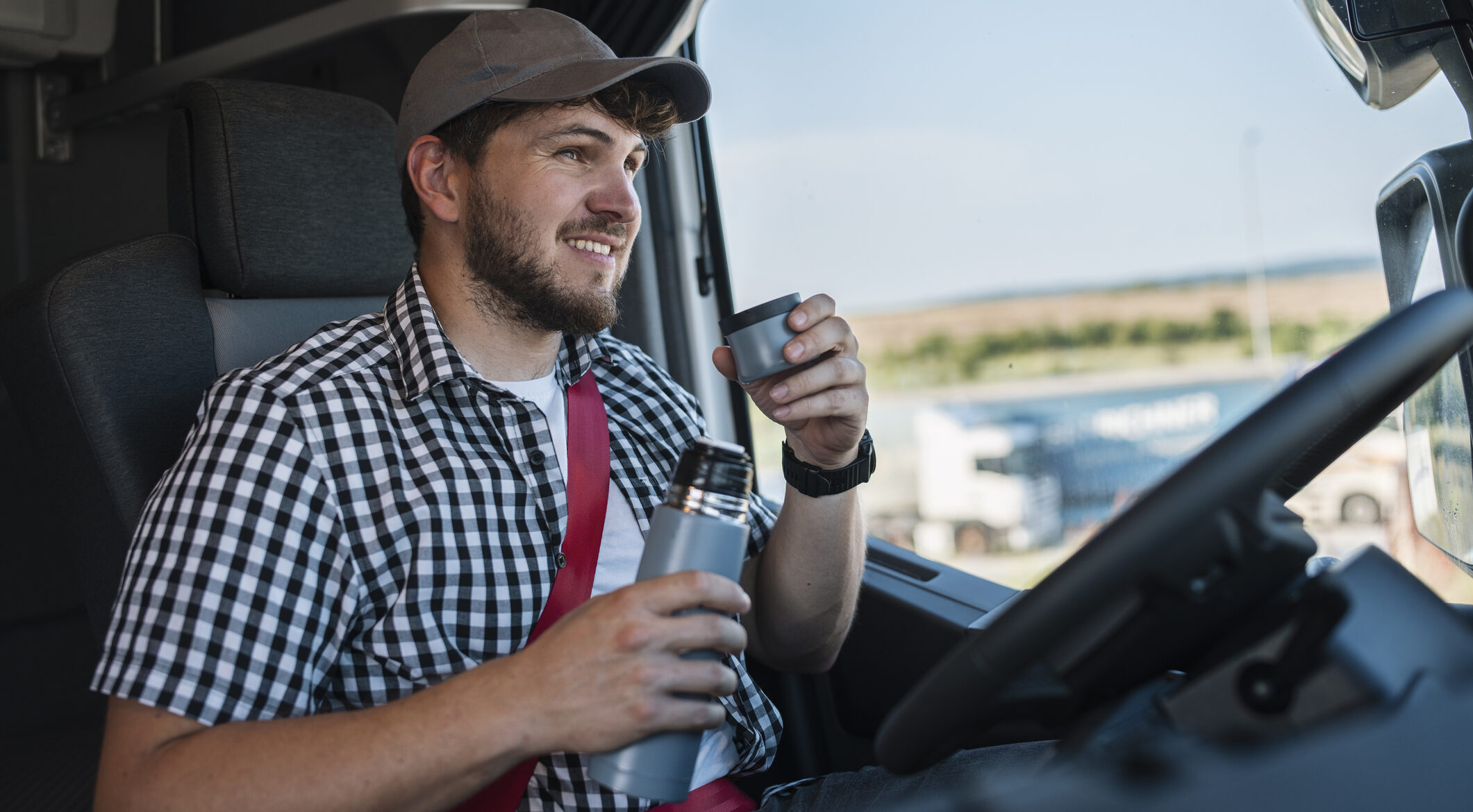 Positive truck driver drink coffee in his cabin.
