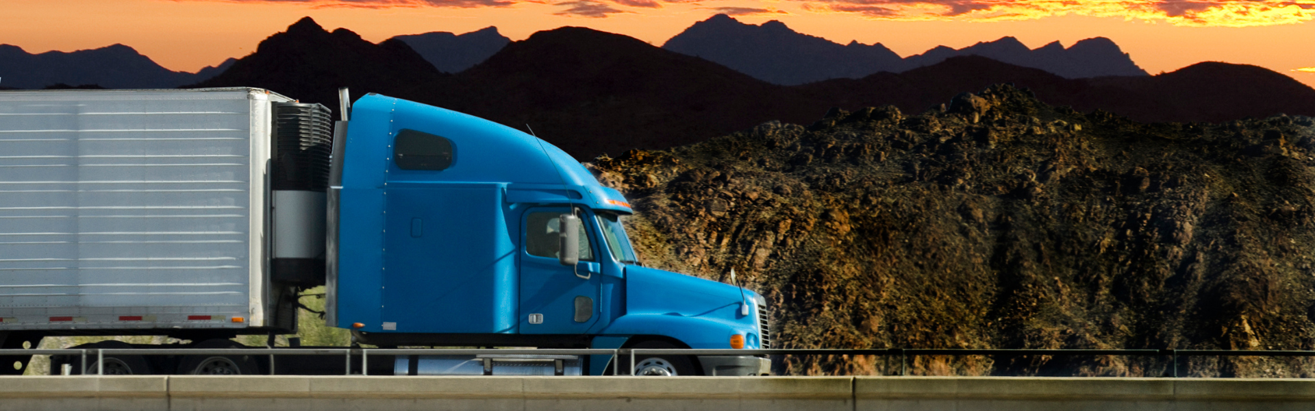 Semi truck crossing bridge with mountains and sunset in background