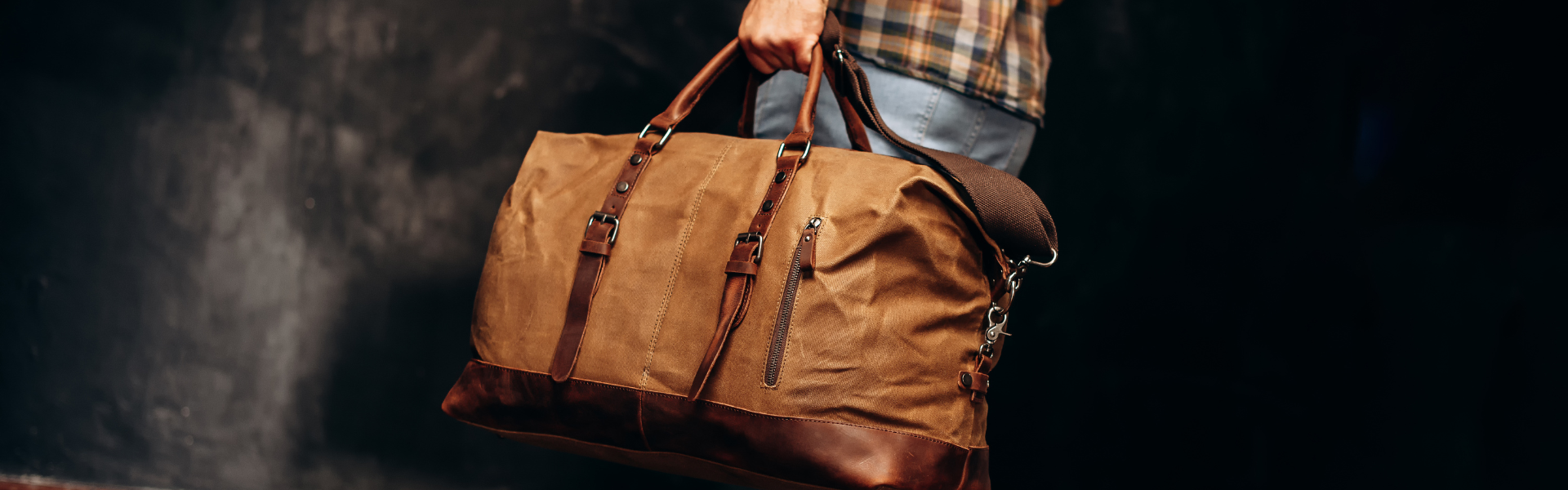 man in jeans and flannel shirt carrying small duffel bag