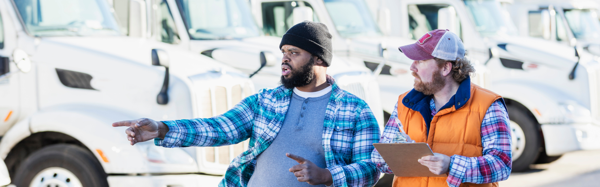 two men in front of a row of parked semi trucks