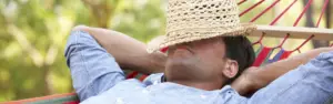 man relaxing in hammock with straw hat over face