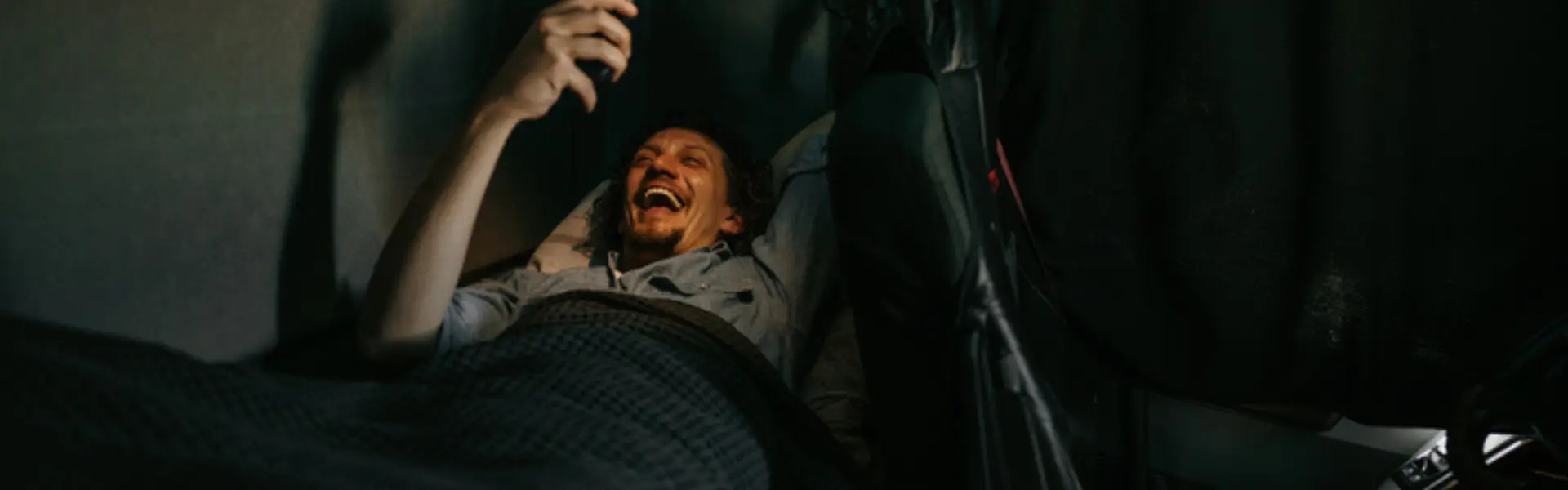 man in sleeper laughing as he looks at phone