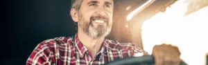 man with salt and pepper beard and hair behind the wheel of a semi truck