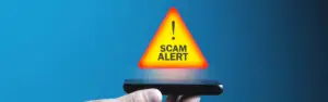 man holding phone with a scam alert icon hovering above it on a blue background
