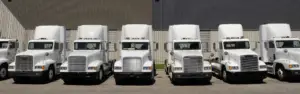 white semi trucks parked in a line in front of a metal building