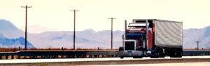 red semi truck with white trailer on bridge with mountains in background