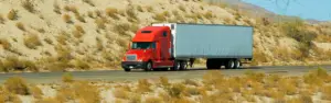 red semi truck pulling white trailer on desert road
