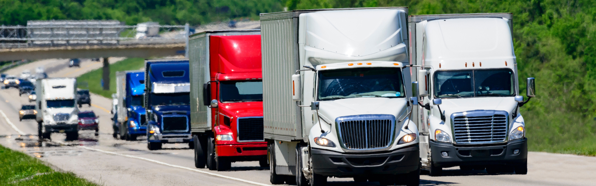 several semi trucks of varying types driving on highway