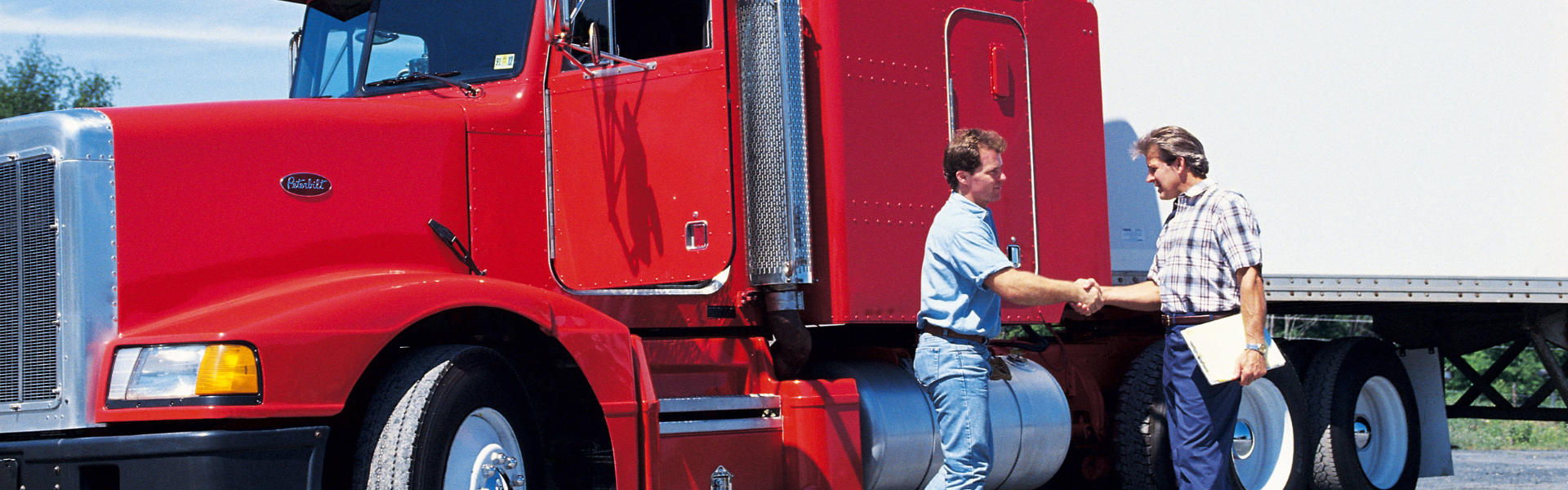 men shaking hands with red semi truck in background
