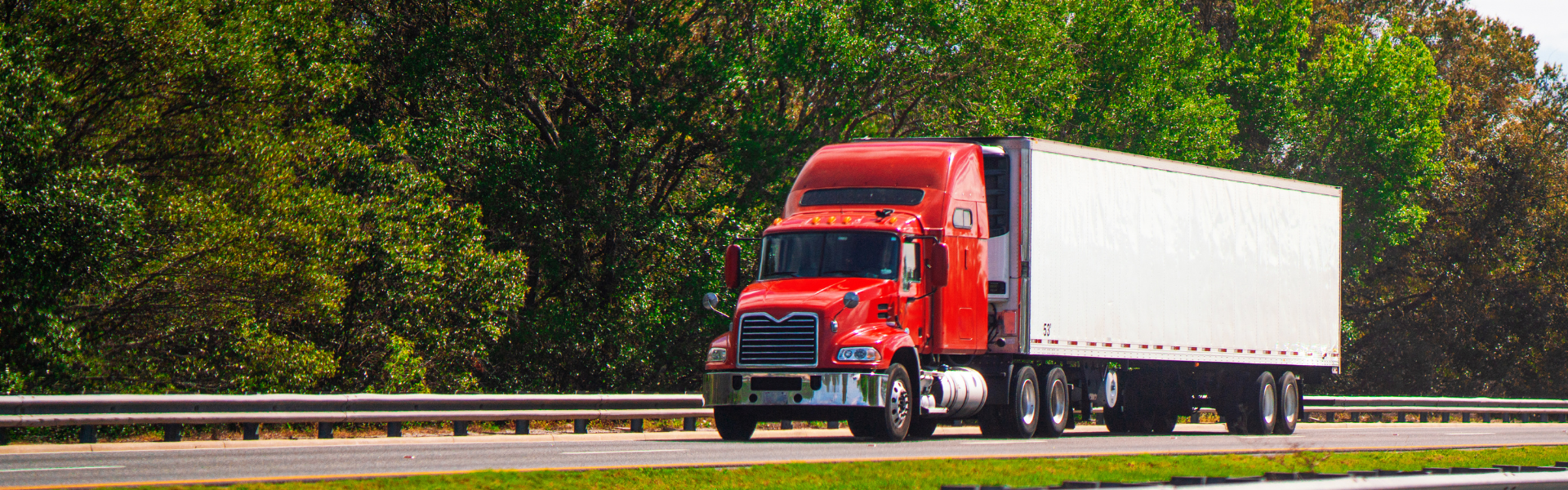 red semi truck pulling white trailer on road with trees in background