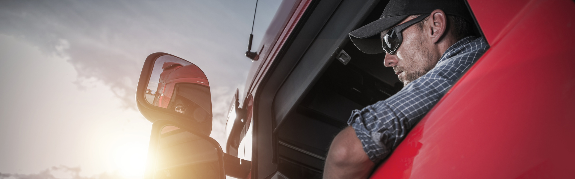 Man wearing hat and sunglasses in cab of red semi truck