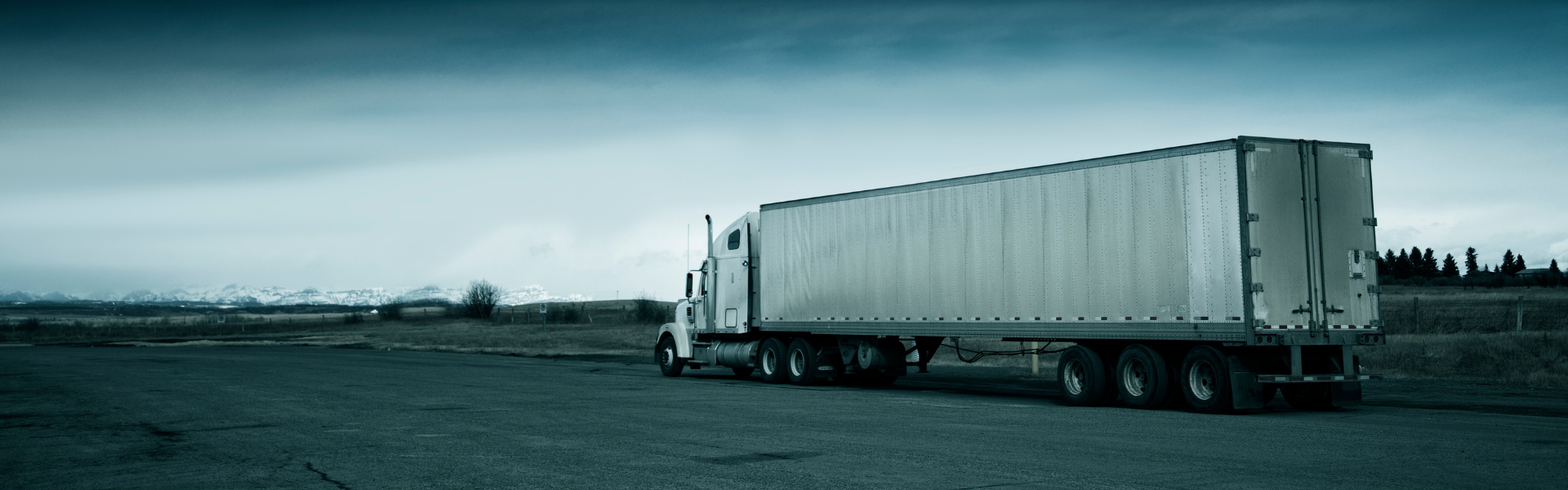 white semi truck pulling white trailer in rural area driving away from camera