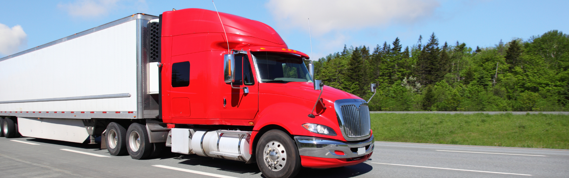 red semi truck with white trailer parked on side of road with trees in background