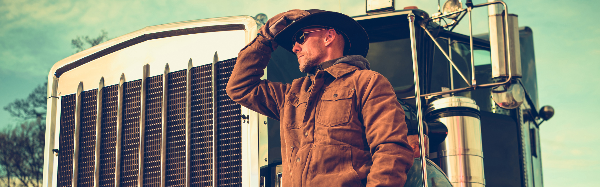 man in work jacket and cowboy hat standing in front of semi truck