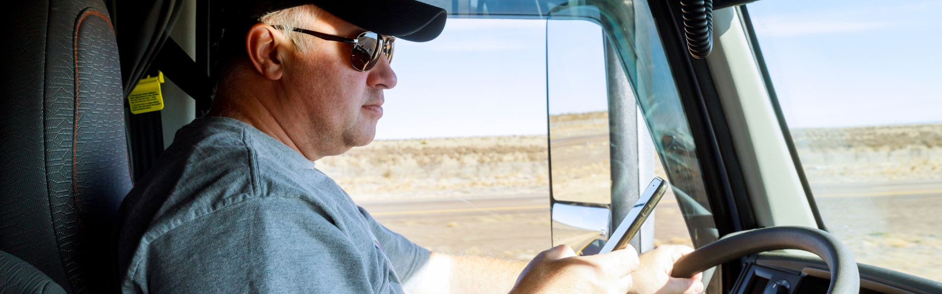 Man sitting in semi truck cab looking at smartphone