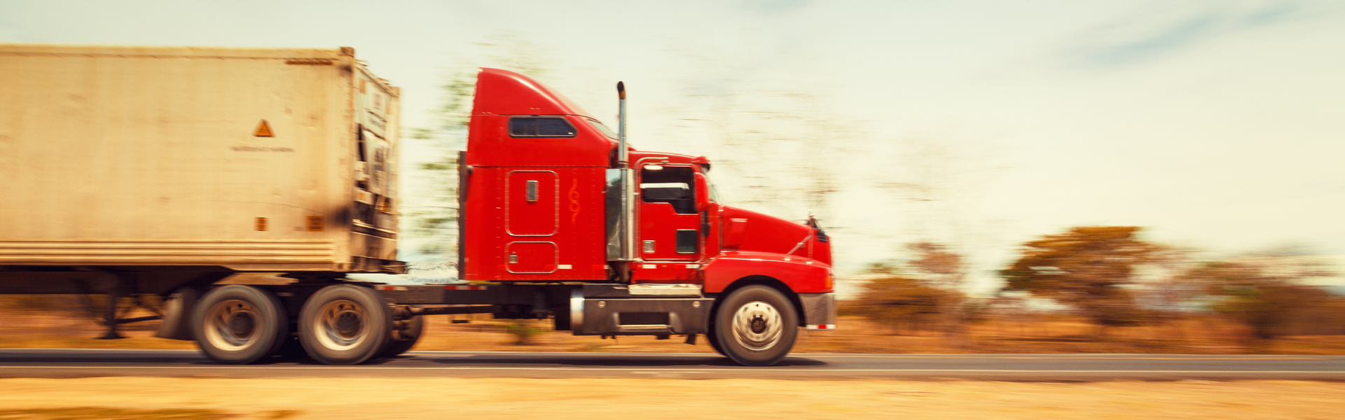 red semi truck pulling white trailer in desert landscape