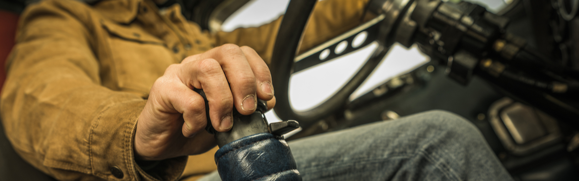truck driver in cab with one hand on steering wheel and one hand on gear shift