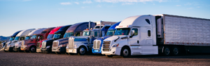 semi trucks of varying types parked in a line in a parking lot