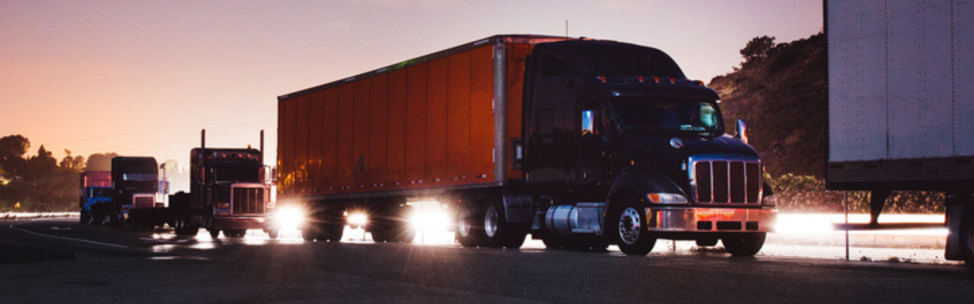 several semi trucks on the road at dusk