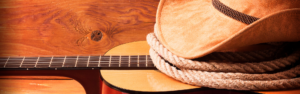 acoustic guitar, cowboy hat, and rope on wood background